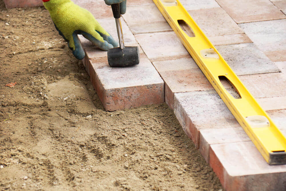 a landscaping Ballarat worker laying a brick path with a mallet to level it off and a yellow strait edge next to him